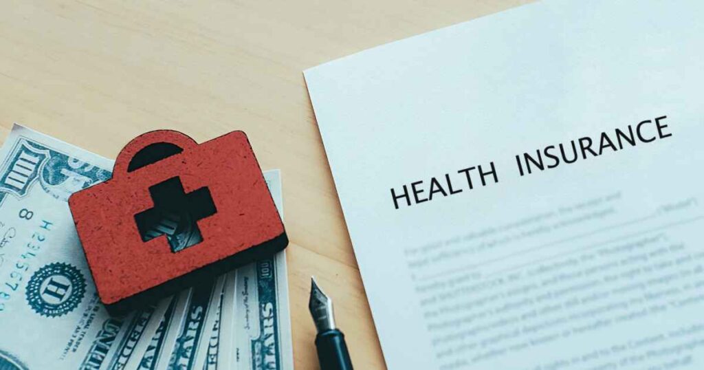 dollar notes and pen beside a health insurance policy 